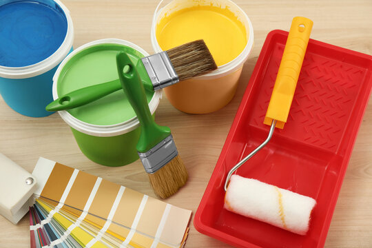 Buckets of paints, palette and decorator's tools on light wooden background, above view