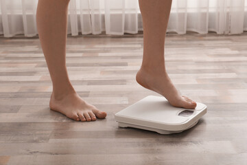 Woman stepping on floor scales indoors, closeup. Weight control