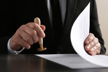 Male notary stamping document at table, closeup