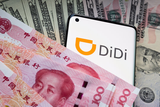 Didi Chuxing Technology company logo seen on smartphone which is covered in chinese Yuan and US dollar banknotes. Concept. Stafford, United Kingdom, July 26, 2021.