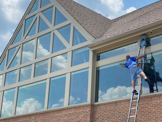 A window washer uses a ladder to wash windows.