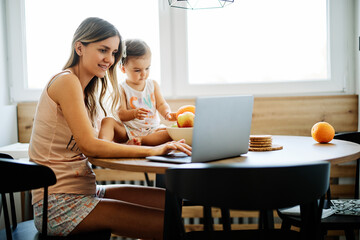 Stay at mother home sitting in kitchen and getting work done while her baby girl helping her.