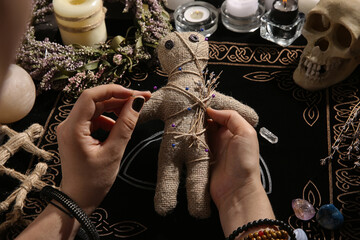 Woman stabbing voodoo doll with needle at table, closeup. Curse ceremony
