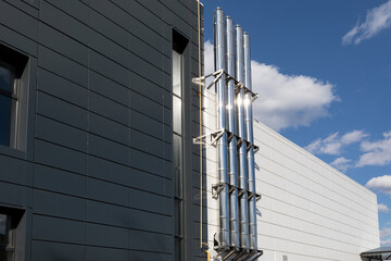 Shiny metal chimney on the outer wall of industrial building against a blue sky background.
