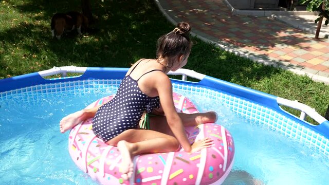Children play in swimming bath floating on donut float on sunny summer day, pool fun