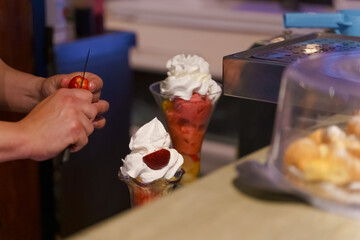 Hispanic man preparing a glass with ice cream, cream and fruits