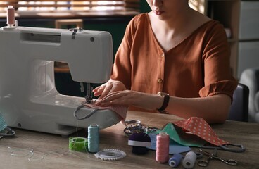 Woman sewing cloth protective mask with machine at table indoors, closeup