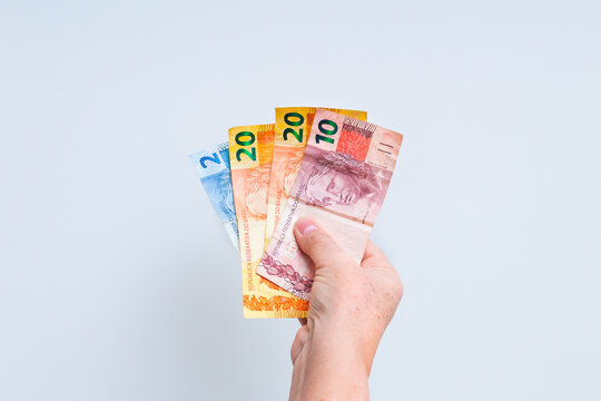 Uma mulher segurando com a mão cédulas do Real - BRL, dinheiro do Brasil, em foto isolada em fundo branco. Pouco dinheiro em forma de leque. Tempo de crise financeira e alta da inflação na economia.