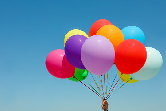 Woman with bunch of colorful balloons against blue sky, closeup