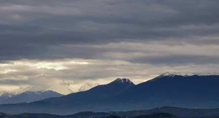 Fototapeta na wymiar Nuvole grigie sopra le montagne innevate