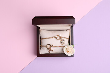 Beautiful jewelry and flower in box on color background, top view