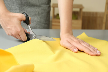 Obraz na płótnie Canvas Seamstress cutting yellow fabric with scissors at workplace, closeup