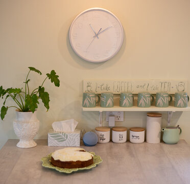 Kitchen Island Bench With Coffee Cups, Clock, Speaker, House Plant And Iced Cake 