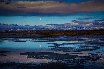 Fototapeta premium Full moon setting as the sun rises over the lake with reflection