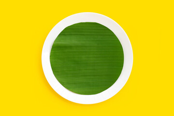 Cut banana leaves into circle shape on plate on yellow background.