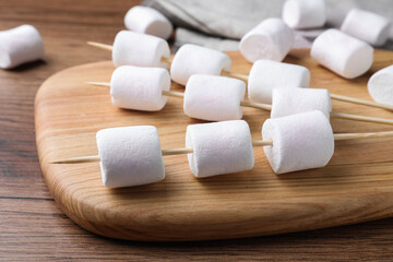 Fototapeta na wymiar Sticks with delicious puffy marshmallows on wooden table, closeup