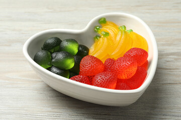 Delicious gummy fruit shaped candies on white wooden table
