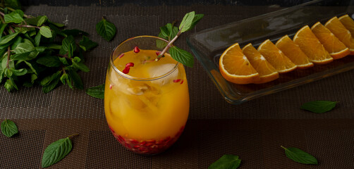 Bebida de Naranja con menta, hielos y granada sobre una mesa de color cafe con rodajas de naranja en un plato