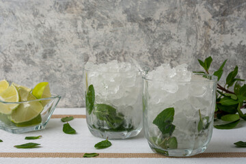 Mojito servido en vaso de cristal con rebanadas de limon y hojas de menta, sobre una mesa de color blanco y fondo vintage