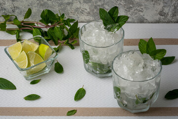 Mojito servido en vaso de cristal con rebanadas de limon y hojas de menta, sobre una mesa de color...