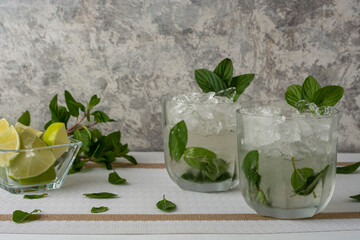 Mojito servido en vaso de cristal con rebanadas de limon y hojas de menta, sobre una mesa de color blanco y fondo vintage