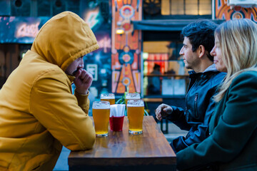 group of three young Hispanic latinos, outside a restaurant bar, drinking beer