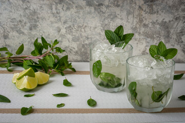 Mojito servido en vaso de cristal con rebanadas de limon y hojas de menta, sobre una mesa de color...