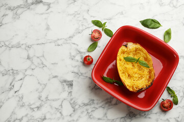 Half of cooked spaghetti squash in baking dish, tomatoes and basil on white marble table, flat lay. Space for text