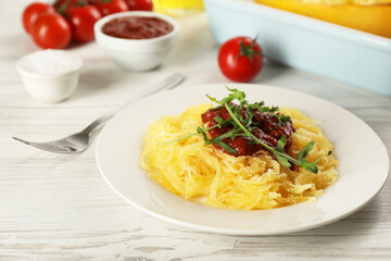 Tasty spaghetti squash with tomato sauce and arugula served on white wooden table, closeup