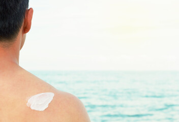 Smear sunscreen on male back against the sea, rear view.