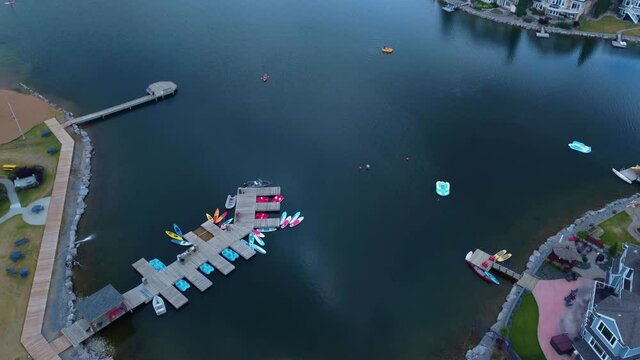 Reveal aerial flyover parking lot next to waterfront launch area for water crafts with docked paddle boats kayaks canoes surfboards and mansions with private docks stone edges and boaters paddling 1-3