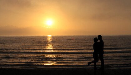 Fototapeta na wymiar Lovers on the beach at sunset. happy Couple Kissing and hugging in Front Of Sun and sea waves. Romantic Lover Concept 