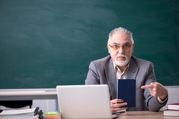 Old male teacher in front of blackboard