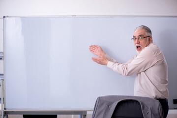 Old male teacher in front of whiteboard