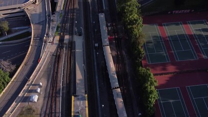 A MBTA red line train leaves a station near a tennis court.