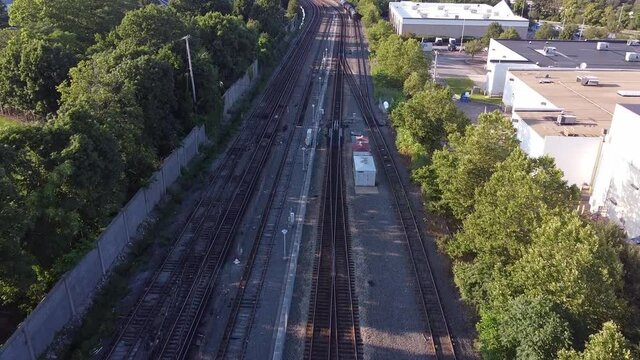 Flying low over empty train tracks near a shopping center, a residential area and a highway.
