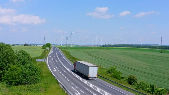 Large White Transport Truck driving on a country road with huge ecological Wind Farm in background