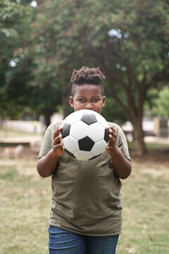 African American boy holding soccer ball and covering his face outdoors in the park