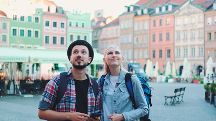 Young couple of tourists using smartphone and admiring beautiful surroundings. They going sightseeing early in the morning.