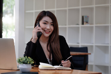 Obraz premium Asian business woman making a phone call and smiling look at camera. secretary famale taking note during call consultant