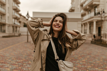 Happy young joyful brunette woman enjoys walk outside. Attractive lady in good mood poses at street and smiles sincerely.