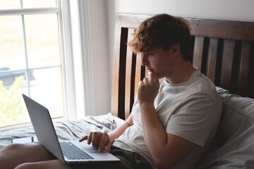 Young man sitting on bed using laptop computer