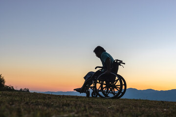 Silhouette Disabled handicapped man is sitting in wheelchair at sunset.mountains background