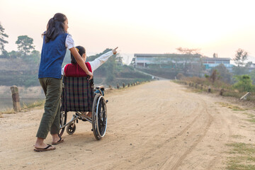 Disabled handicapped woman in wheelchair and care helper walking on trail