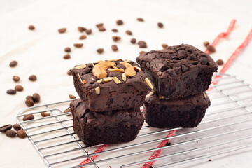 4 square dark brownies with chocolate chips, almonds and nuts on a baking rack, coffee beans placed on a white cloth, side view.