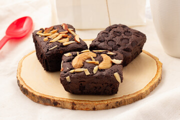 3 square dark brownies with chocolate chips, almonds and nuts on a wooden saucer, sweets for tea time, coffee time, or break time.