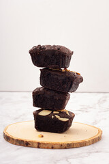 Side view of 4 square dark brownies with chocolate chips, almonds and nuts on a wooden saucer, stack of brownie, sweets for tea time, coffee time, or break time.
