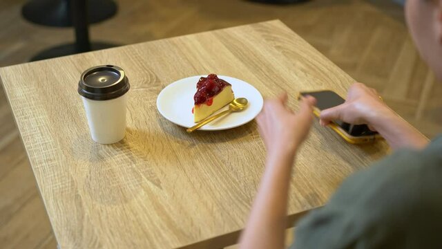 4K Asian woman using smartphone photography tasty cheesecake dessert on the table at coffee shop. Female blogger photographing sweet bakery cake and beverage for advertising small business restaurant