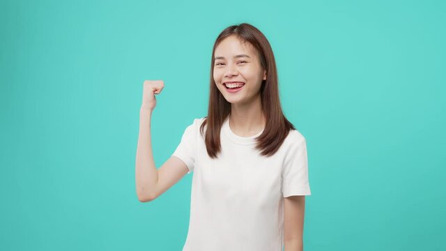 Studio shot of cheerful beautiful Asian woman in a white t-shirt and stand come here gesture with hand inviting welcoming on blue background.