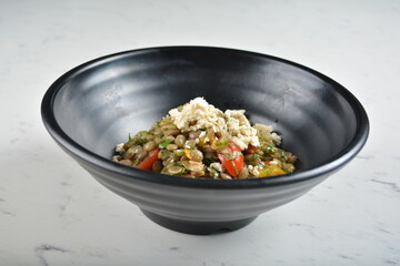trio quinoa grain salad bowl with avocado, tomato, pea bean, carrot and brown rice in black bowl in...